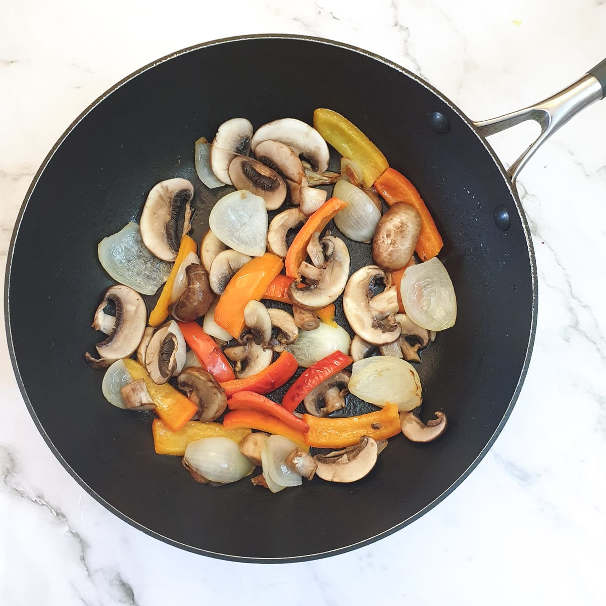 Red pepper slices, onions and mushrooms frying in a pan.