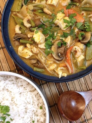 A pan of Thai red curry seafood next to a dish of jasmine rice.