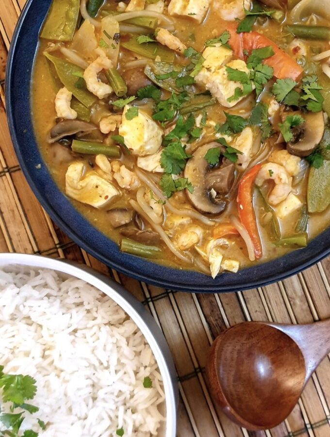 A pan of Thai red curry seafood next to a dish of jasmine rice.