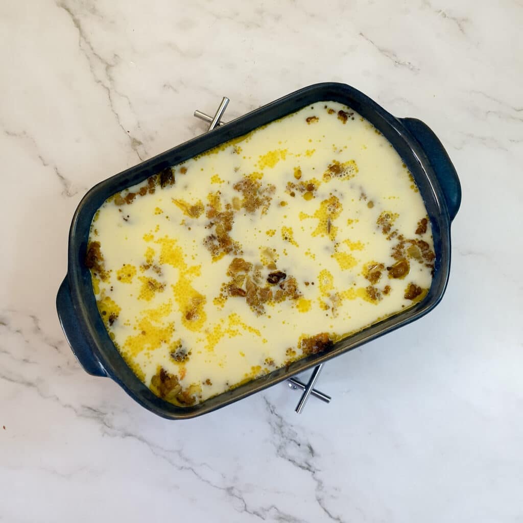 Egg and milk poured over half-baked bobotie in a baking dish.