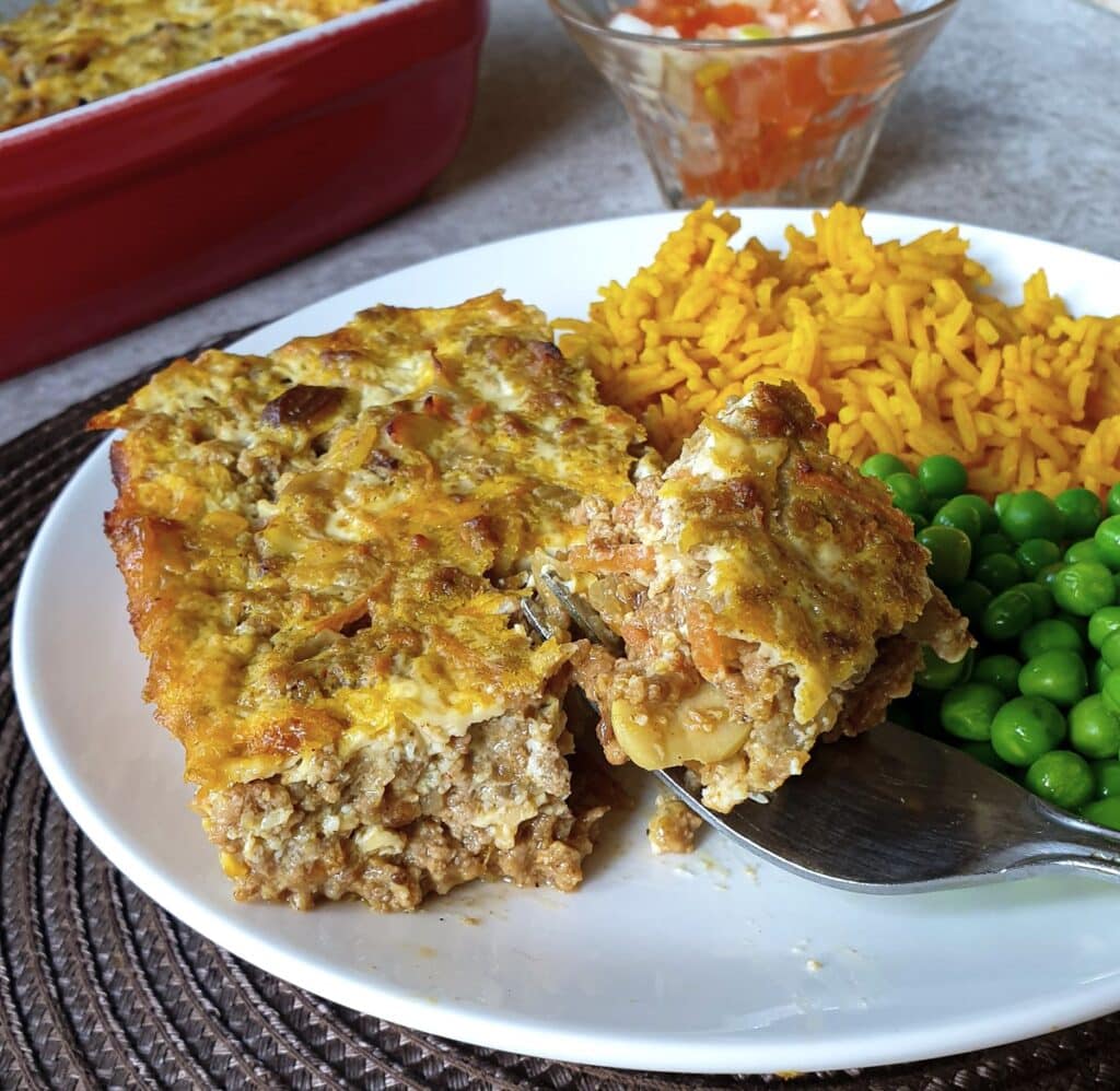 Closeup of a helping of bobotie with yellow rice and peas.