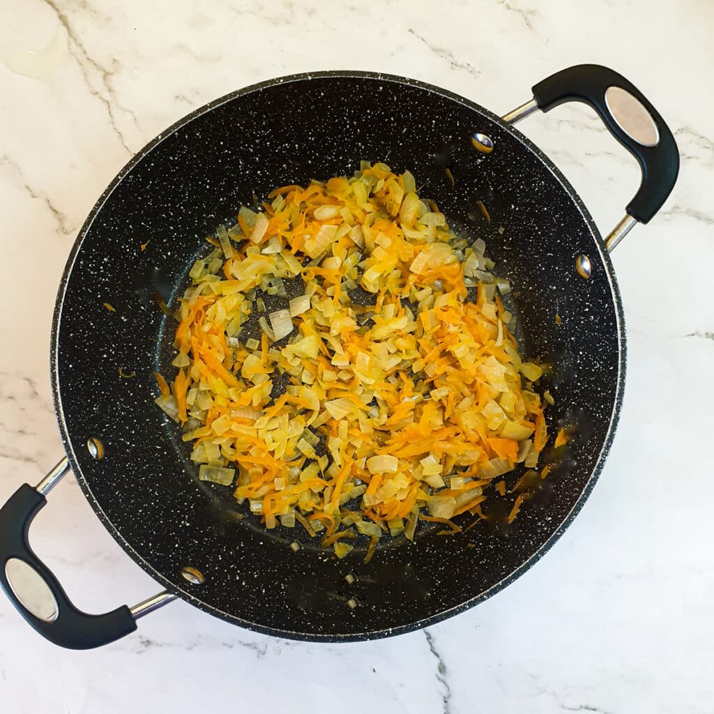 Diced onions and grated carrots frying in a frying pan.