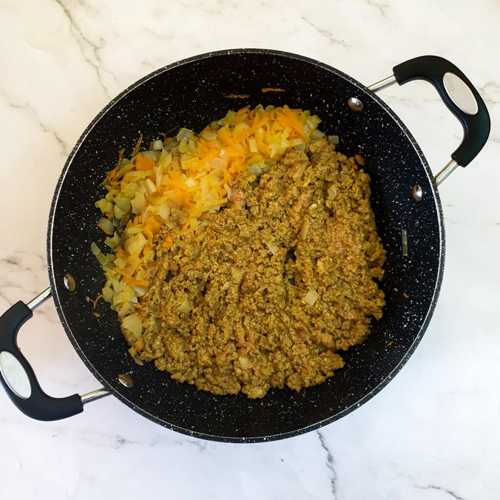 Bobotie mince and spices frying with carrots and onions in a frying pan.