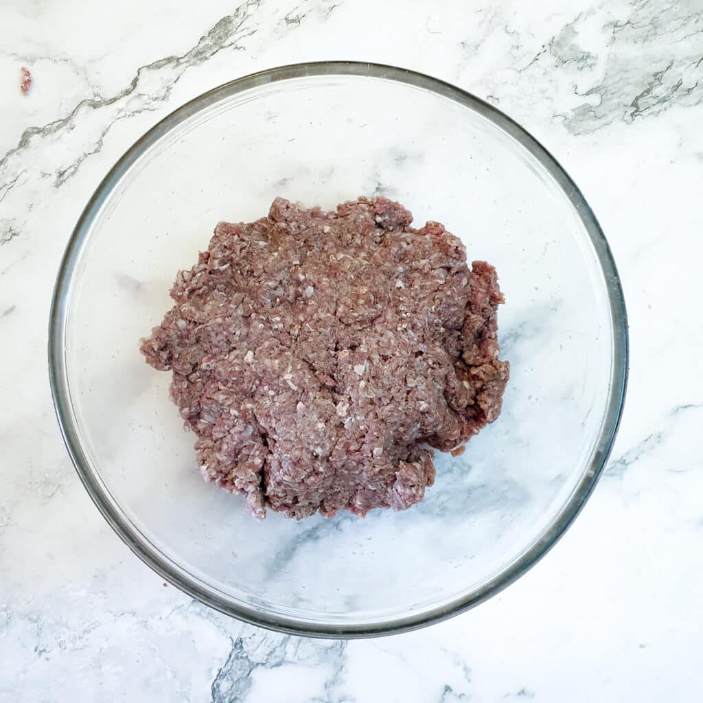 Ground meat and spices combined in a mixing bowl.