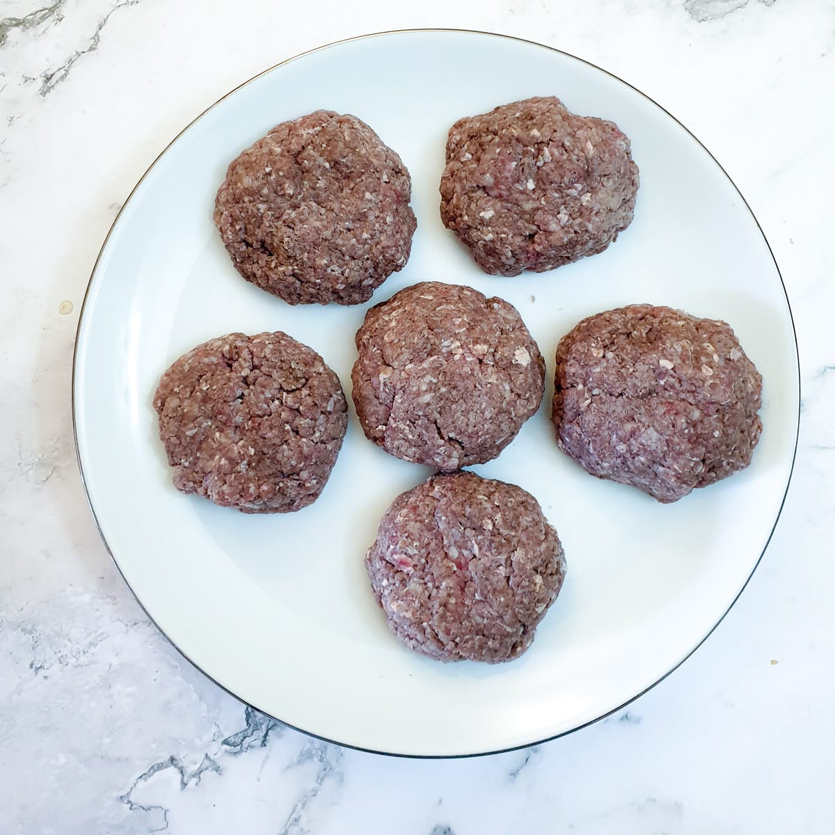 6 raw boerewors patties on a white plate.