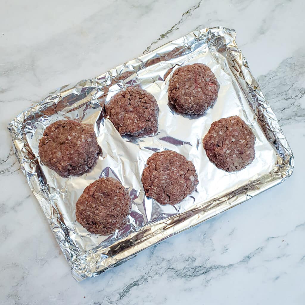 6 raw boerewors patties on a baking tray lined with tinfoil.