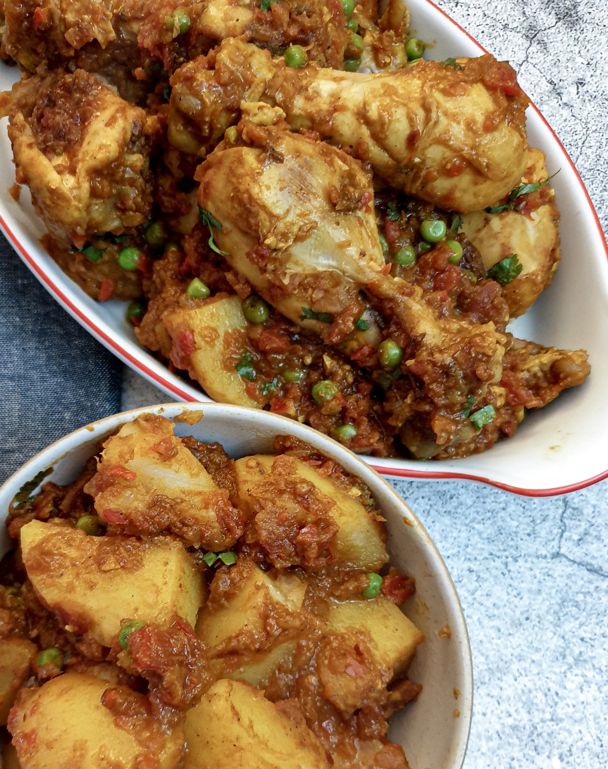 A dish of chicken bhuna made with chicken drumsticks, next to a side dish of Bombay potatoes.