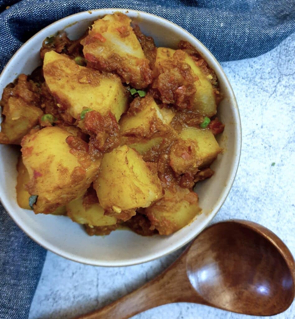 A dish of bombay potatoes next to a wooden spoon.