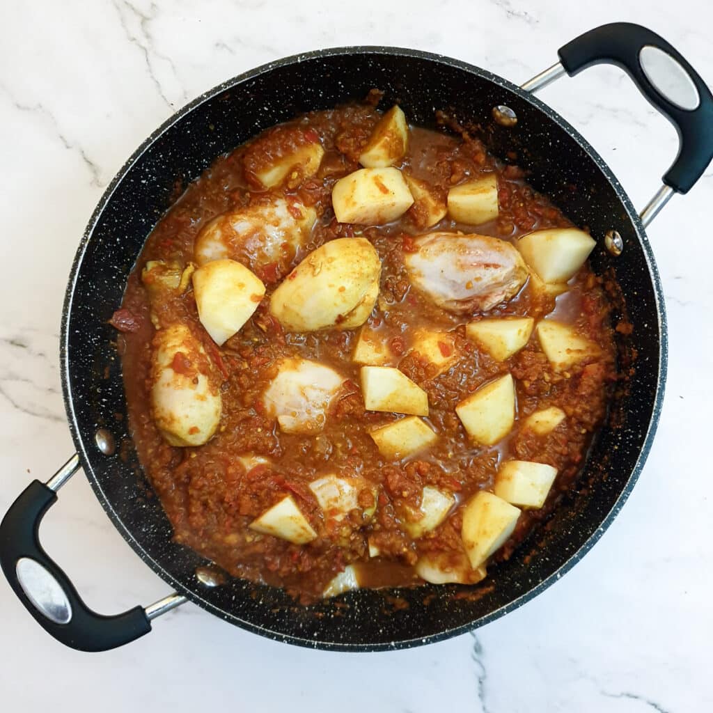 Potatoes added to the chicken and curry paste in a frying pan.