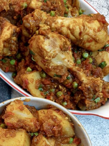 A dish of chicken bhuna made with chicken drumsticks, next to a side dish of Bombay potatoes.