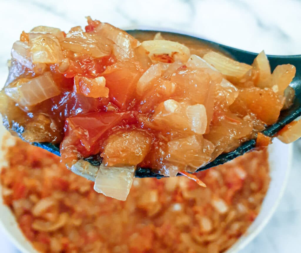 Close up of chilli tomato and onion sauce on a large spoon.