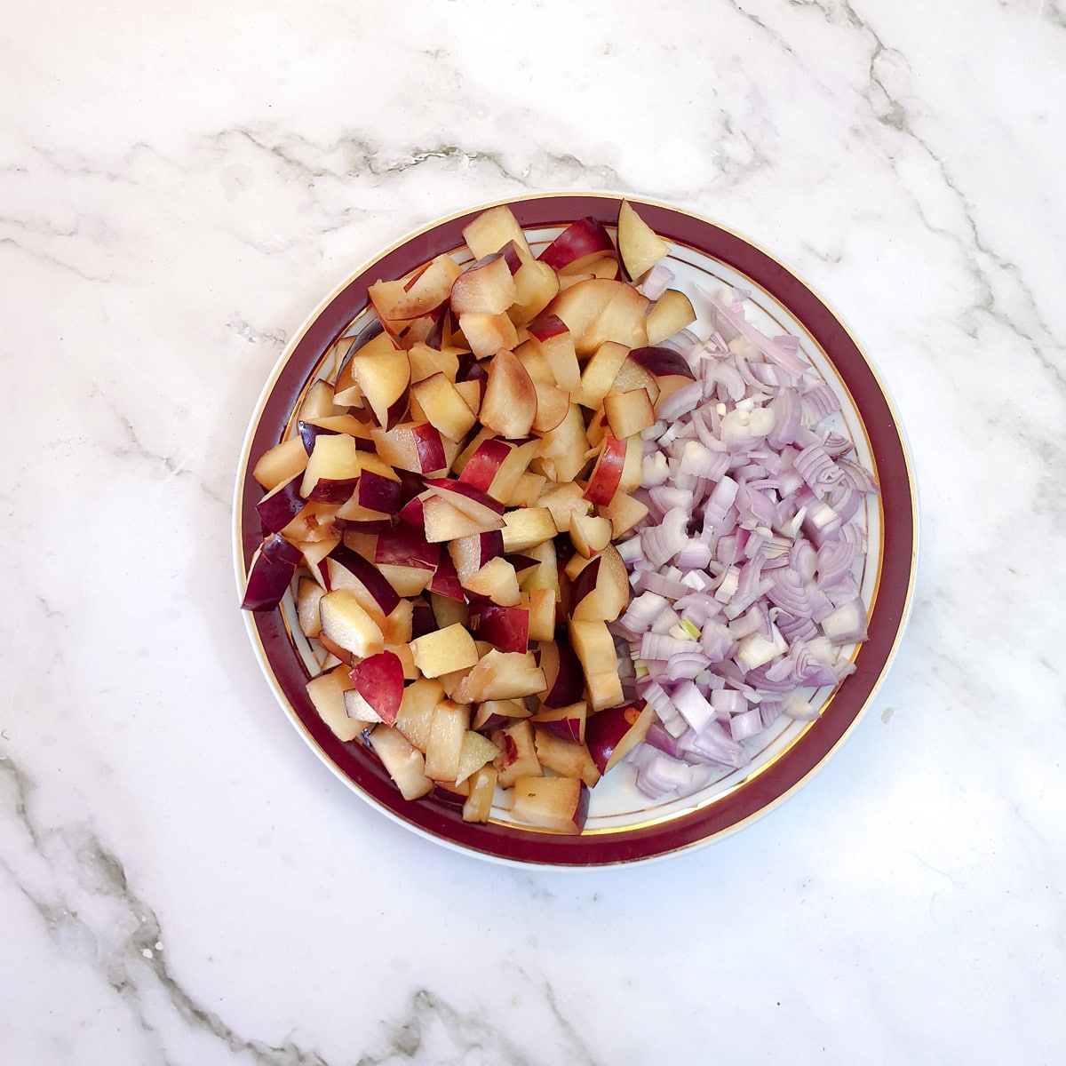 Chopped plums and chopped shallots on a plate.