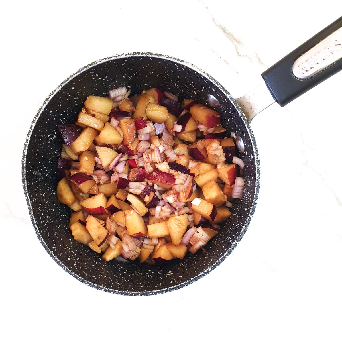 Chopped plums and shallots in a saucepan with sugar and spices.