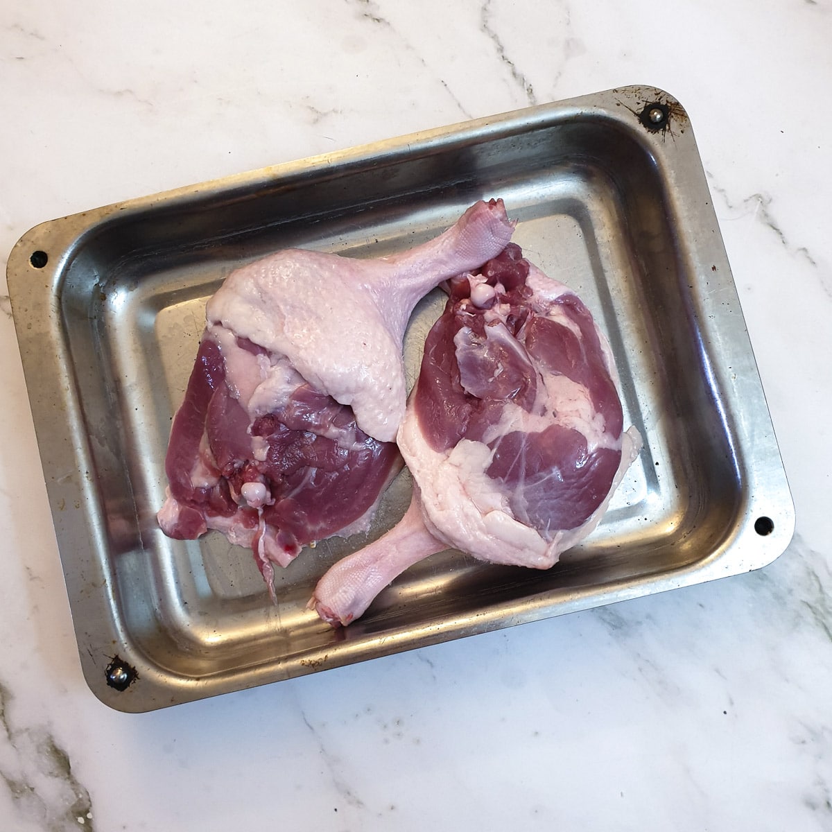 Two uncooked duck legs in a roasting dish.