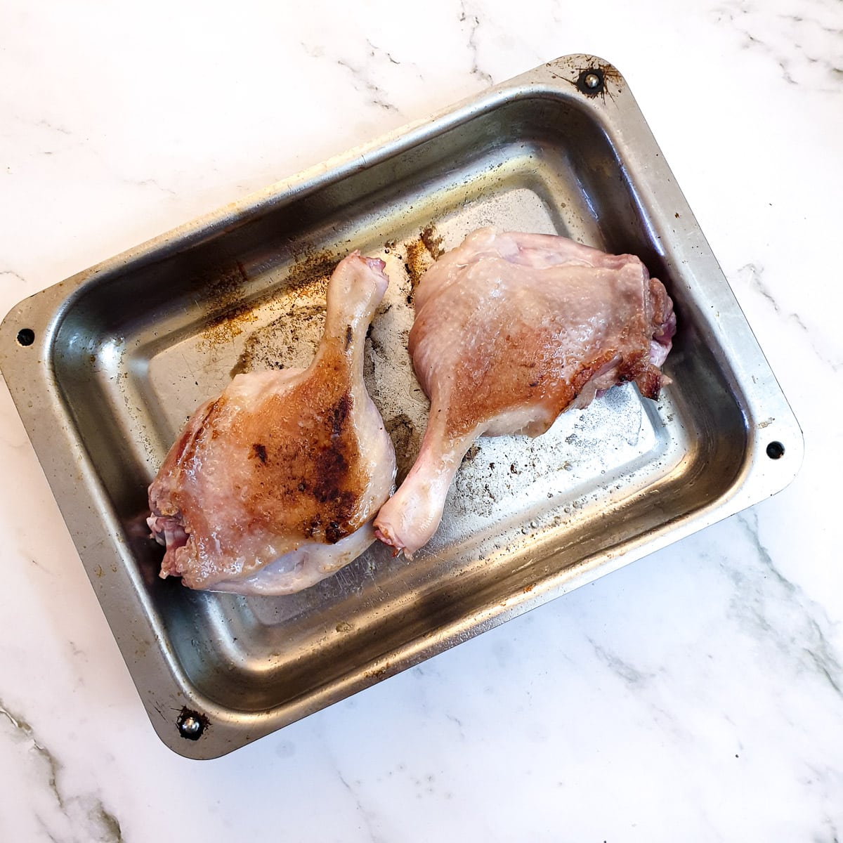 Two duck legs browning in a roasting dish.