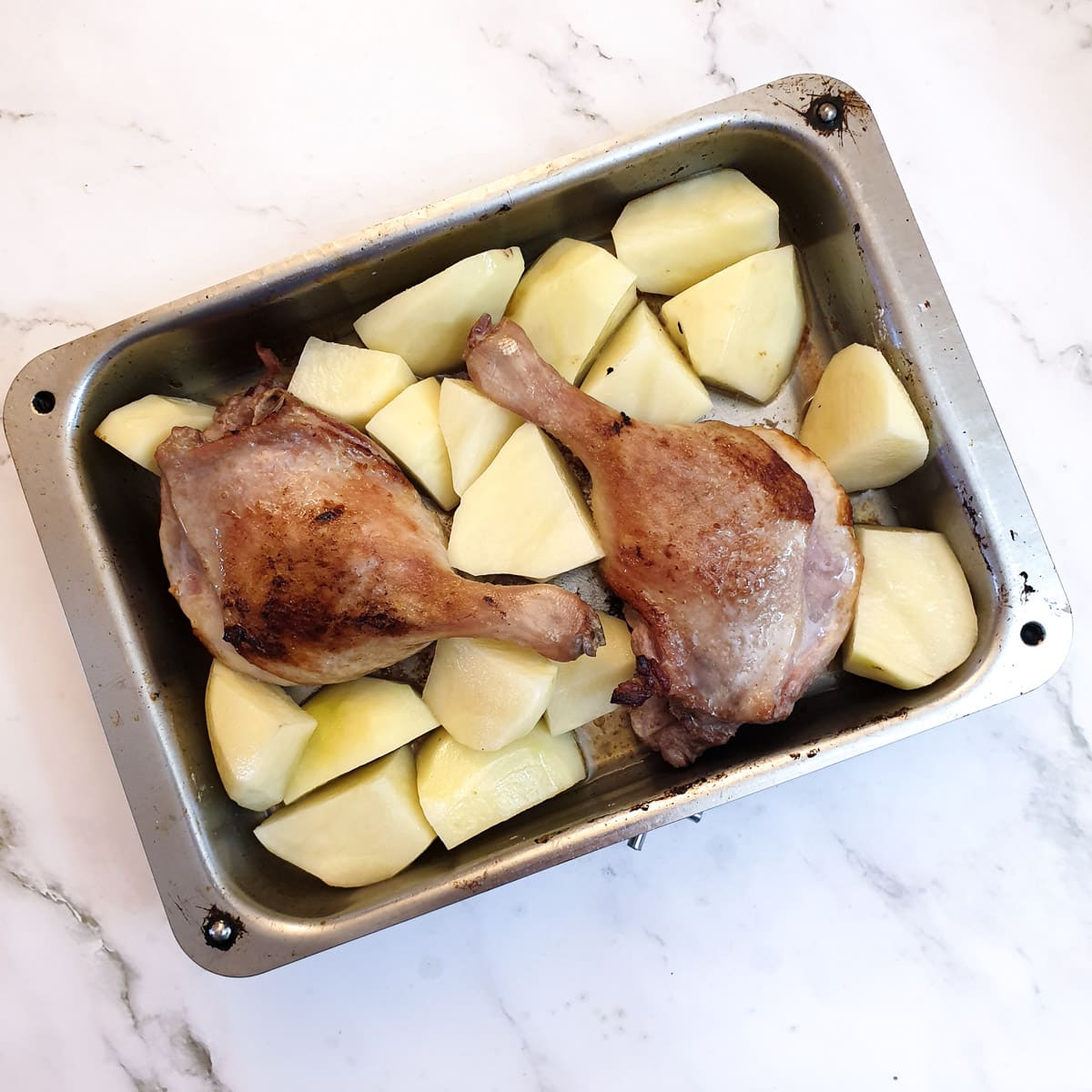 Two duck legs with potatoes in a roasting dish.