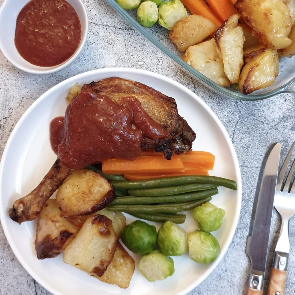 A duck leg smothered with plum sauce on a white plate with vegetables.