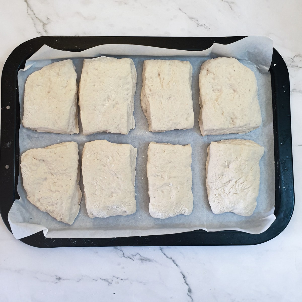 8 unbaked ciabatta rolls on a baking tray.