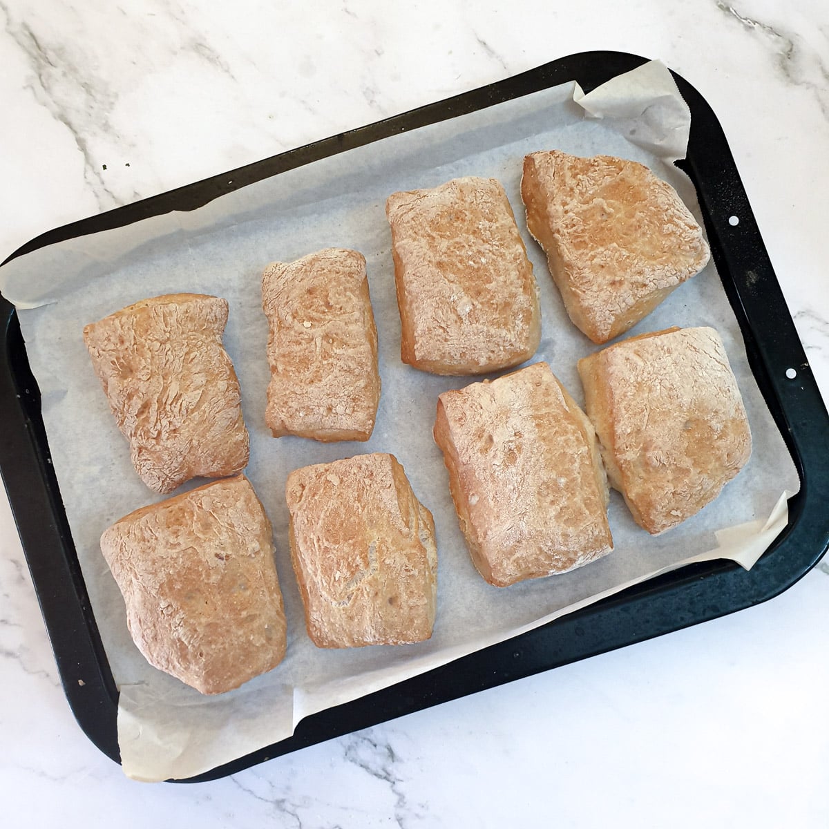 8 baked ciabatta rolls on a baking tray.