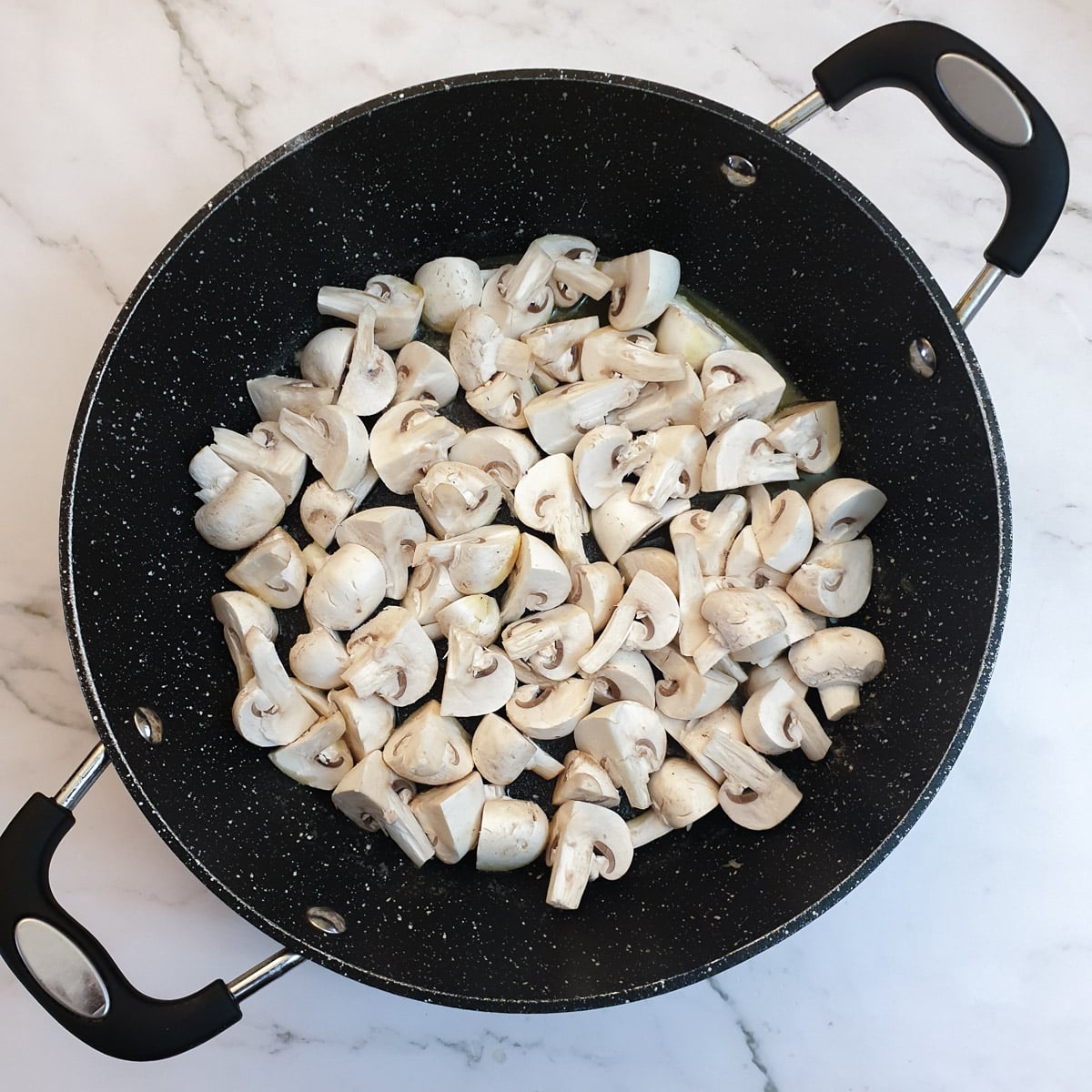 Chopped white mushrooms in a frying pan.