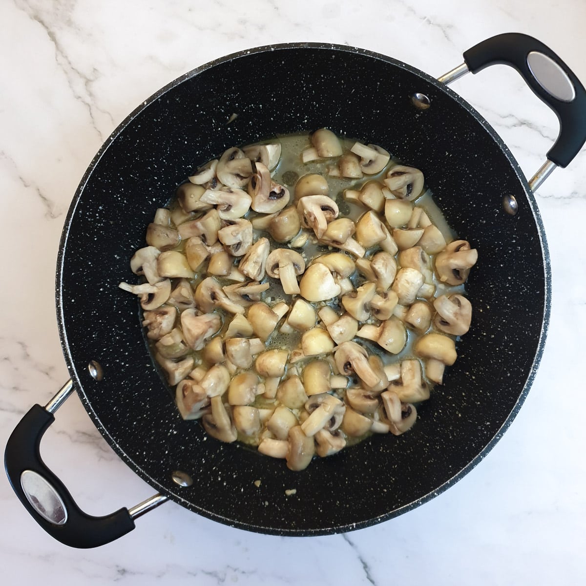 A frying pan containing mushrooms that have released their moisture.