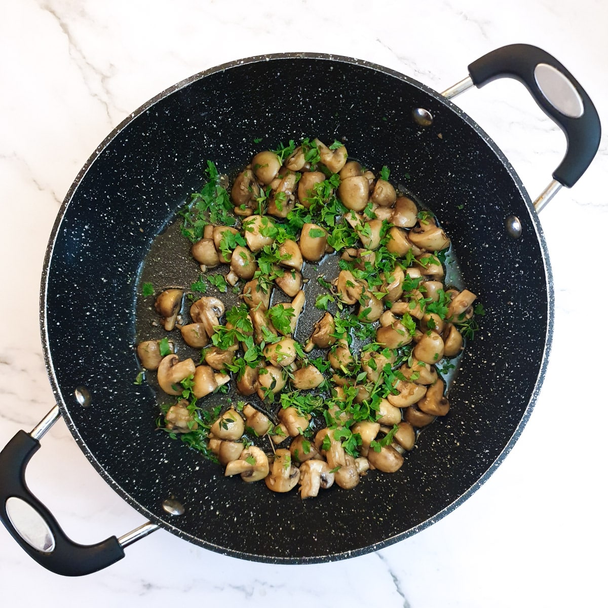 Chopped parsley and thyme added to browned mushrooms in a frying pan.