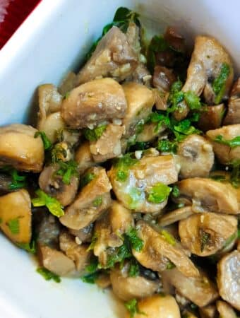 Garlic mushrooms garnished with parsley in a white dish.
