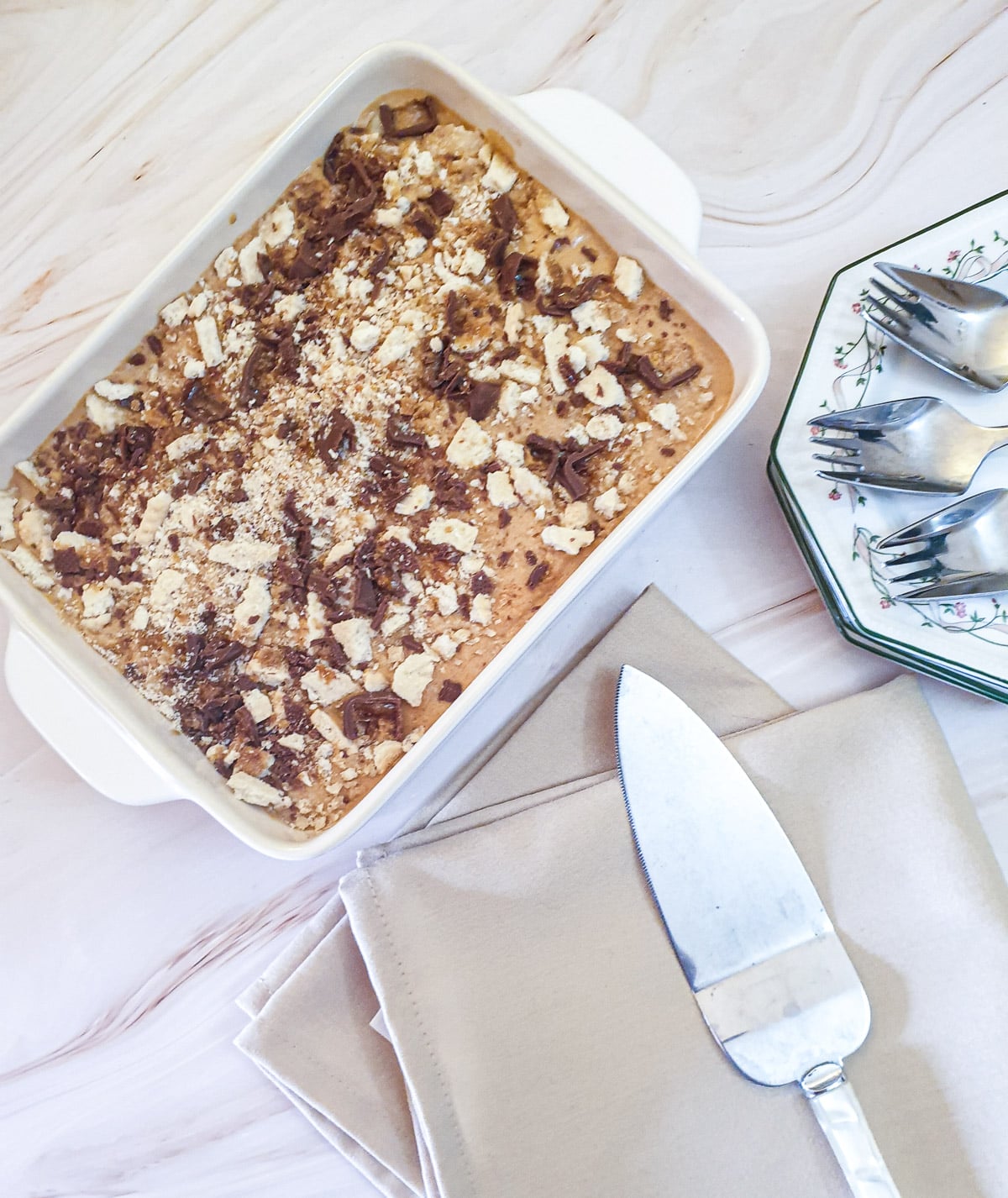 A honeycomb caramel tart in a baking dish next to a beige serviette and a cake lifter.