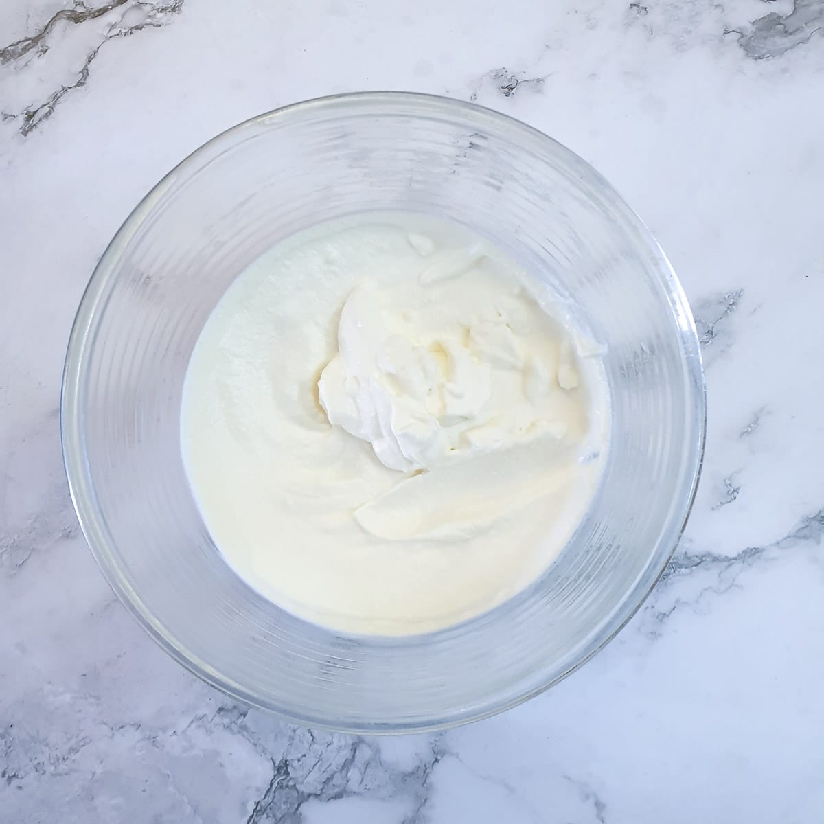 Stiffly whipped cream in a glass bowl.