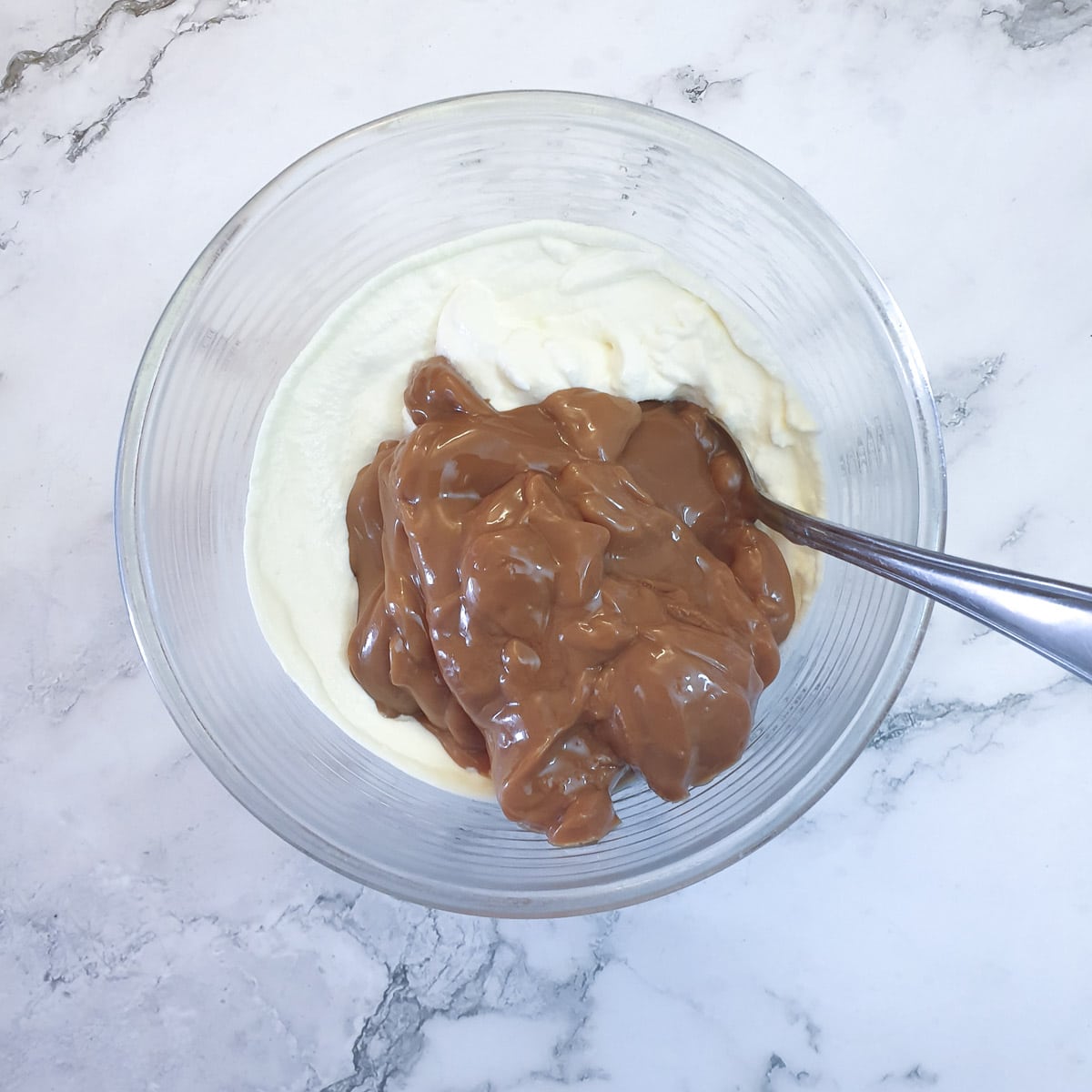 Caramel condensed milk on top of stiffly whipped cream in a glass bowl.