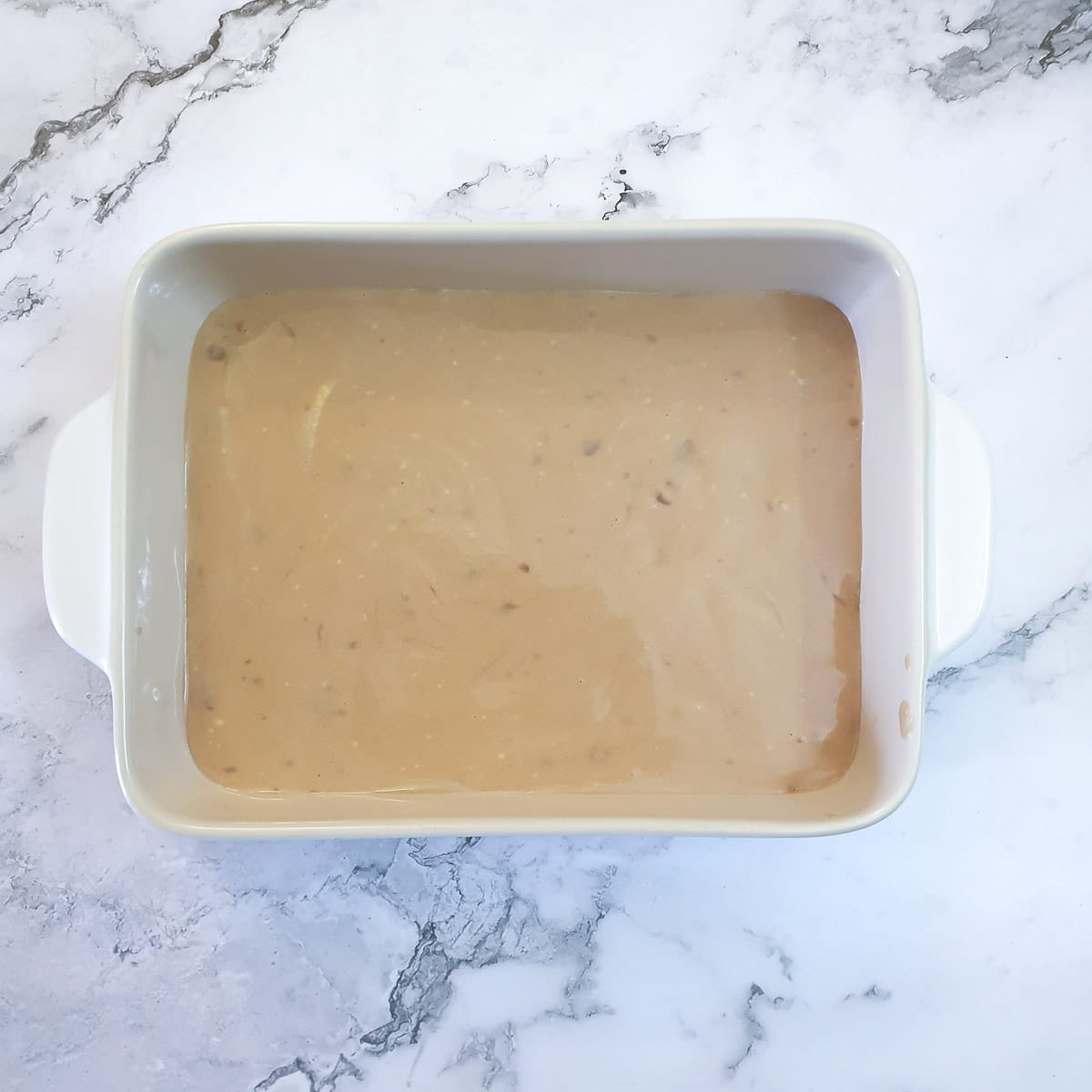 A layer of condensed milk and whipped cream poured over biscuits in a baking dish.