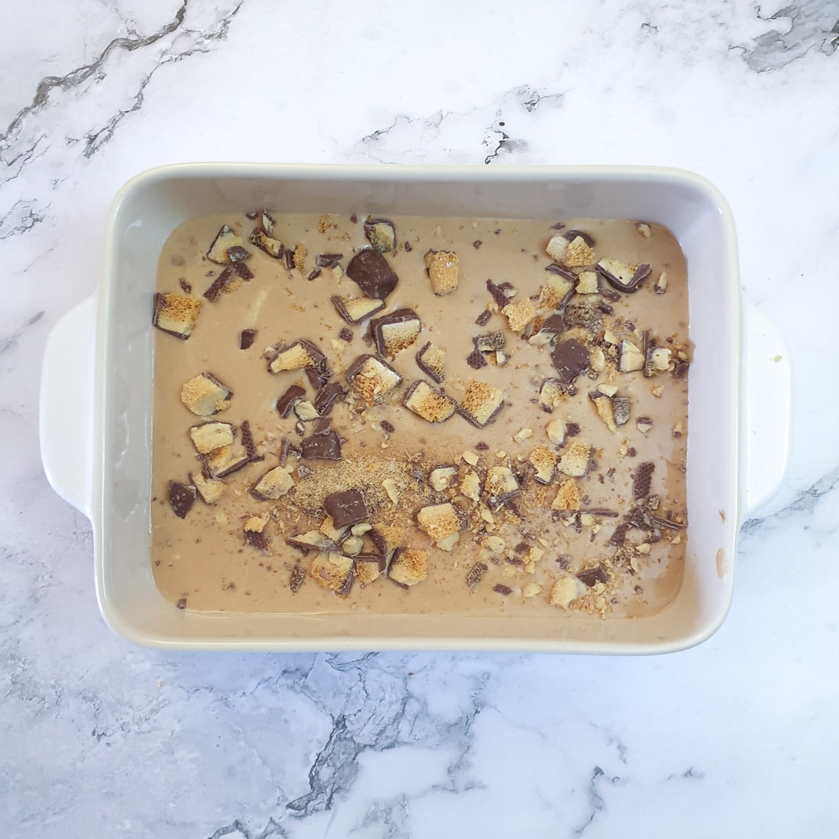 Finely chopped Crunchie chocolate sprinkled on condensed milk and cream in a baking dish.