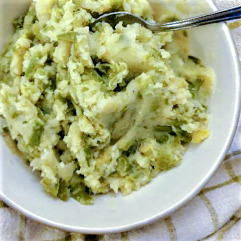 Mashed green beans in a white dish on a green checked cloth.