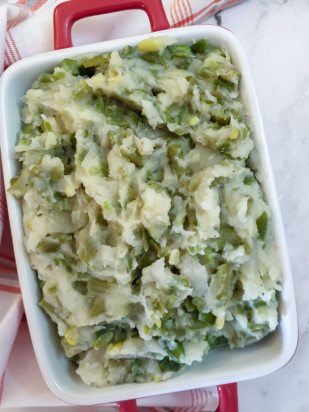 Closeup of a red serving dish filled with mashed green beans.