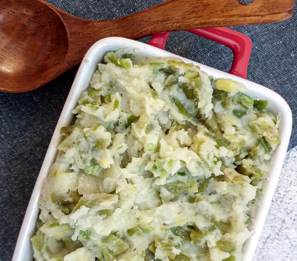 A red serving dish filled with mashed green beans next to a wooden serving spoon.