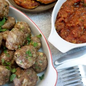 A dish of Moroccan lamb meatballs next to a dish of homemade tomato sauce.