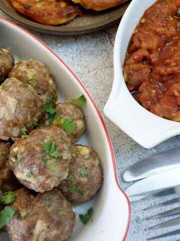 A dish of Moroccan lamb meatballs next to a dish of homemade tomato sauce.