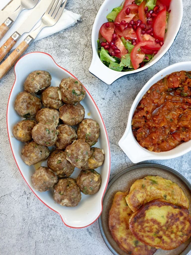 Overhead shot of a dish of Moroccan lamb meatballs, with a dish of tomato sauce and a green salad.