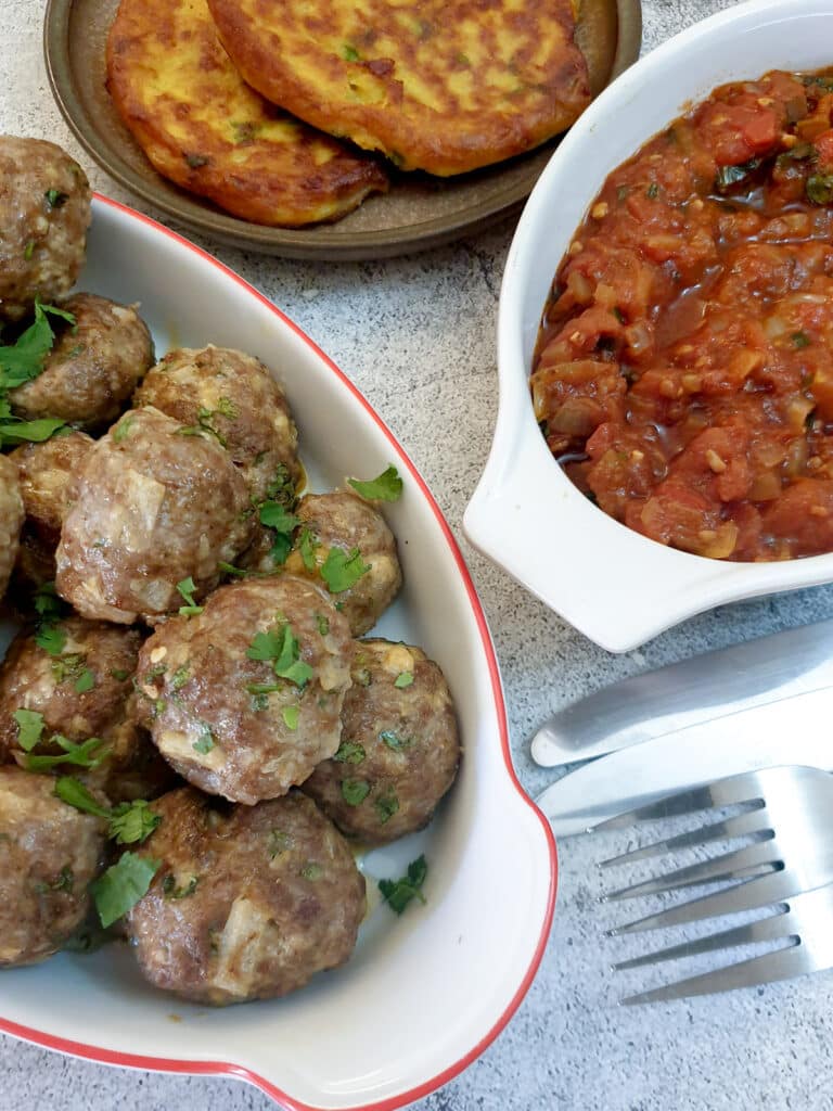 A dish of Moroccan lamb meatballs next to a dish of homemade tomato sauce.