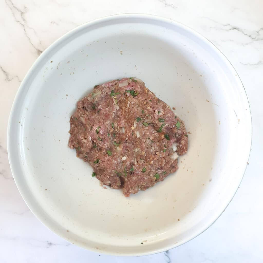 A mixing bowl containing a mixture of meat and spices ready to be formed into meatballs.