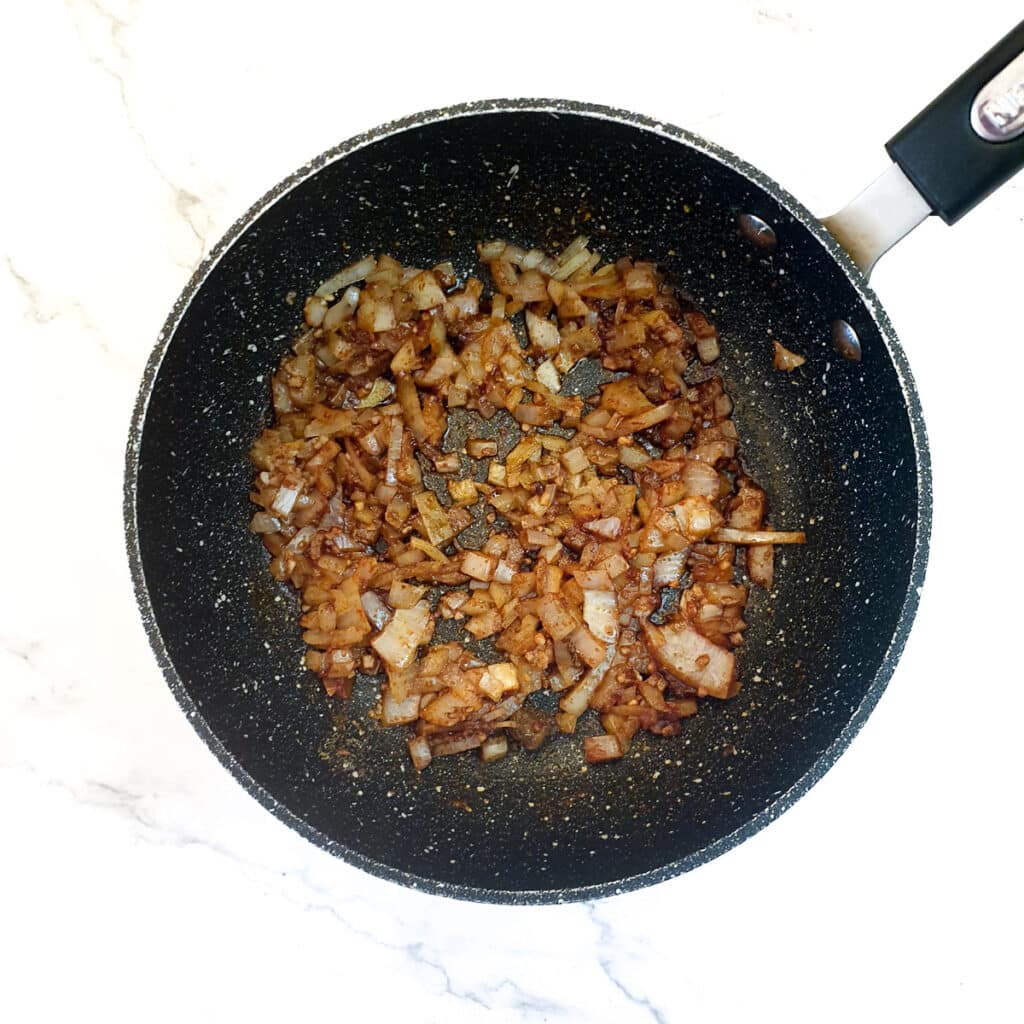 Onions and spices frying in a frying pan.