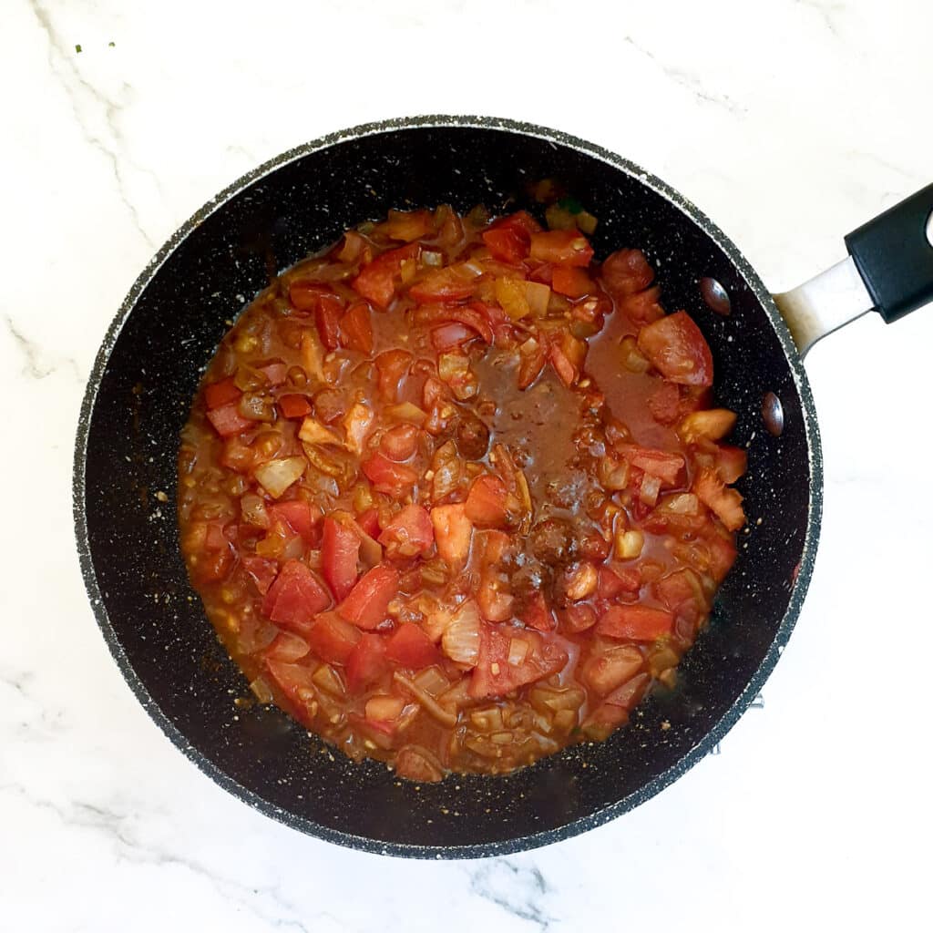 Tomatoes and spices with onions in a frying pan.