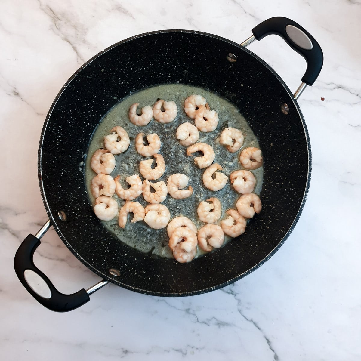 Prawns frying in butter in a frying pan.