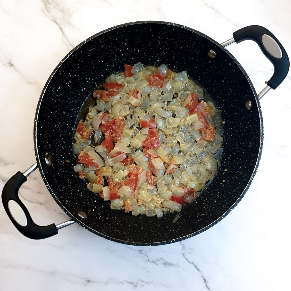 Chopped tomatoes and onions in a frying pan.