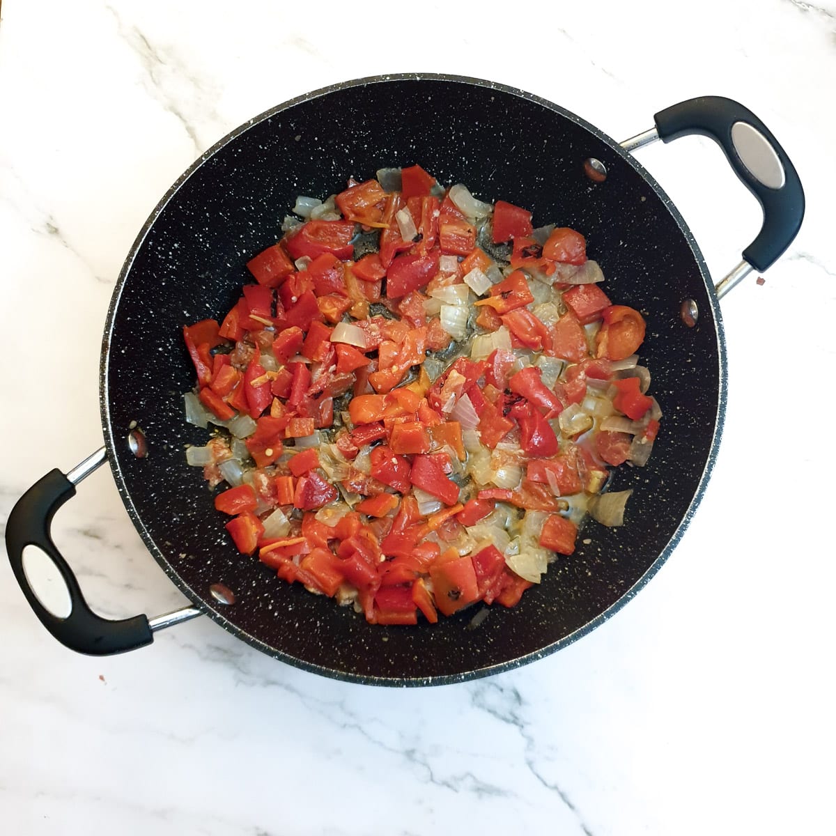 Chopped red peppers with onions and tonatoes in a frying pan.