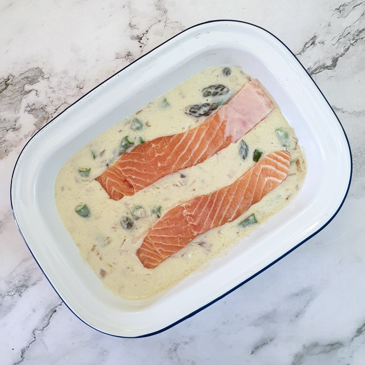 2 salmon fillets nestled in asparagus sauce in an ovenproof baking dish.