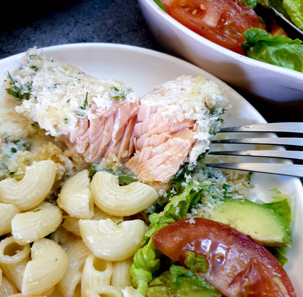 Close up of a piece of flaked salmon on a plate with buttered noodles.