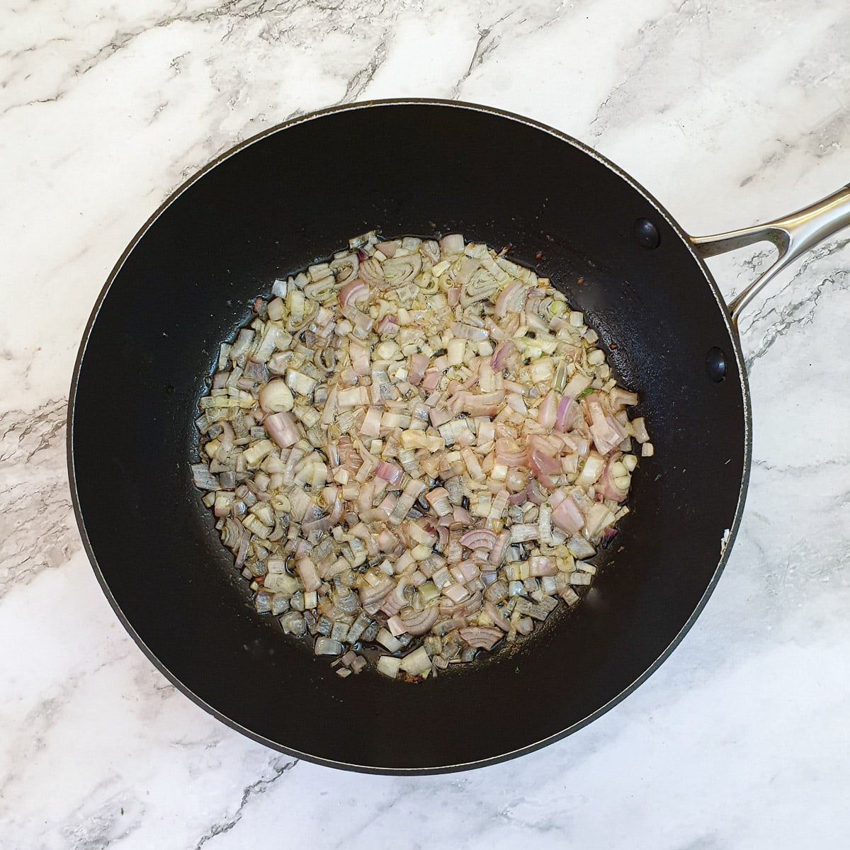 Chopped shallots frying in a frying pan.