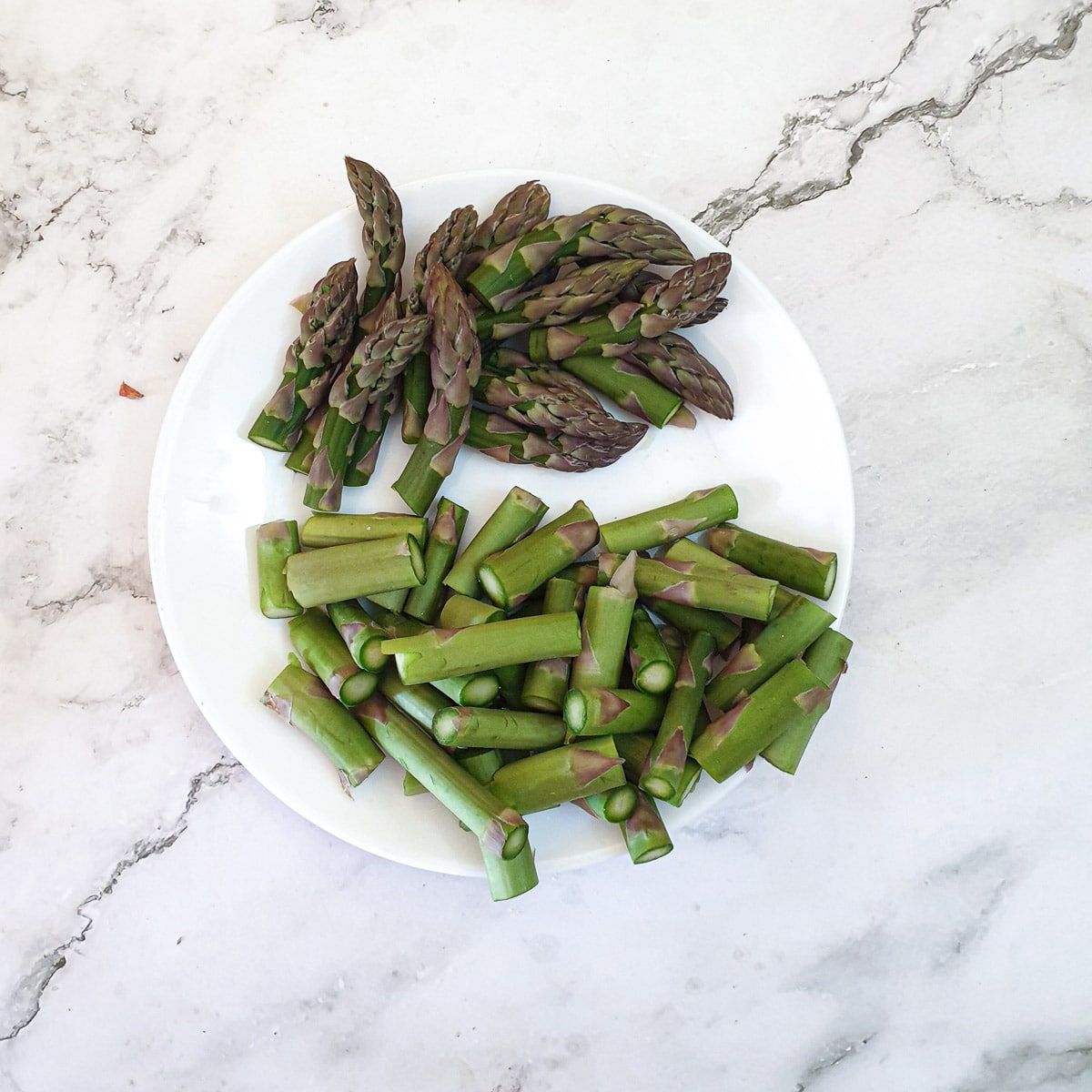 Asparagus stalks and tips cut into short lengths on a white plate.