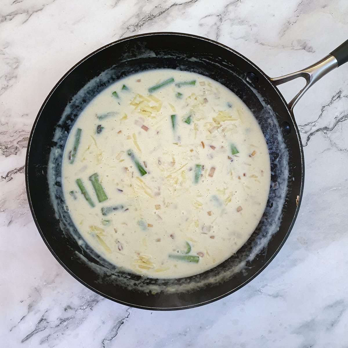 Grated cheddar cheese being stirred into the asparagus sauce.